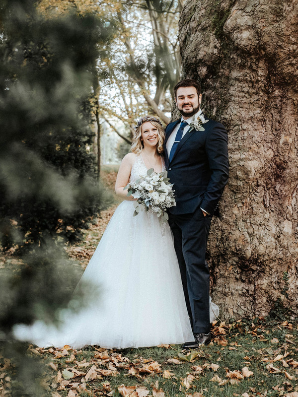 Das Bild zeigt ein glückliches Brautpaar, welches das Brautkleid bei uns im Wuppertaler Brautmodengeschäft erworben hat, posierend im Wald.